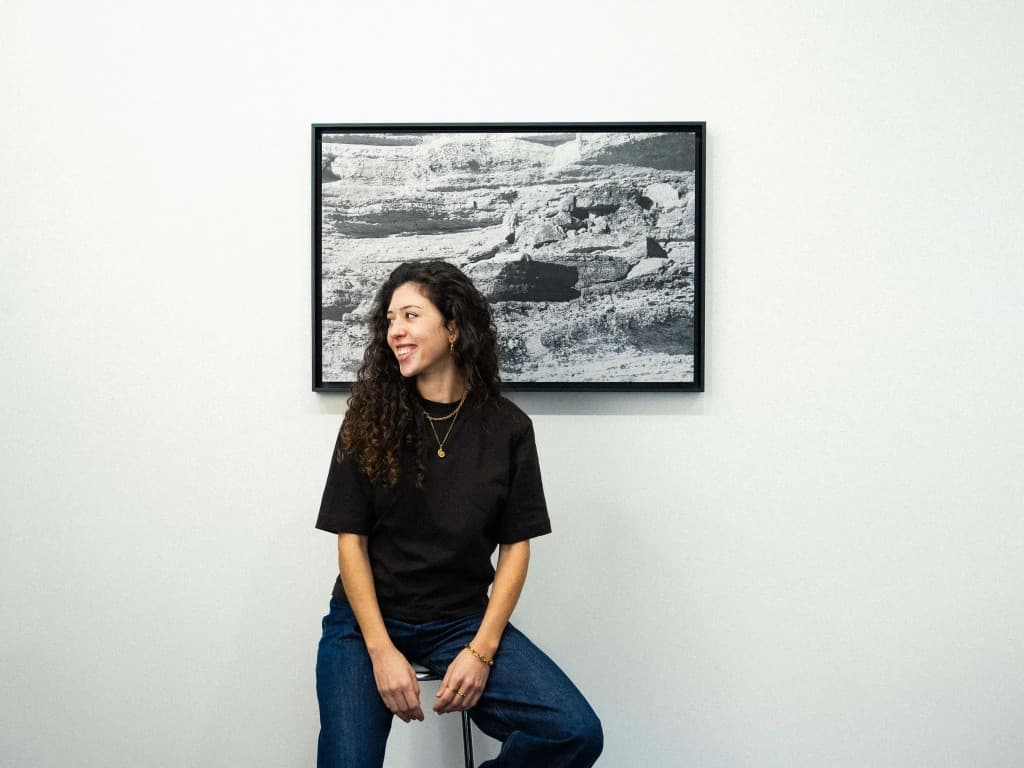 Artist in the studio, seated in front of a framed black-and-white landscape photograph